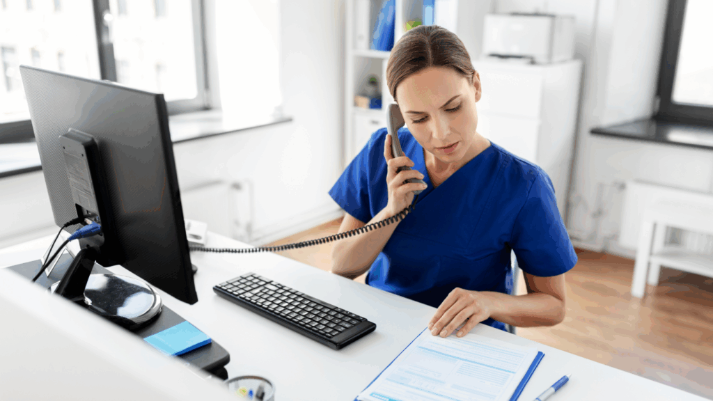 A nurse making a phone call and using the computer at the office desk.