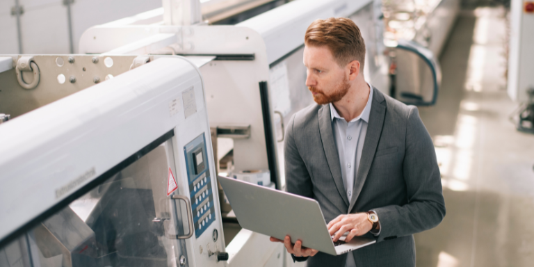 An employee of a manufacturing plant walking the floor and completing quality assurance testing with a laptop.