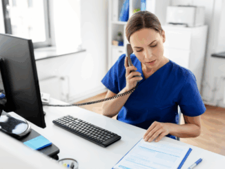 A nurse making a phone call and using the computer at the office desk.