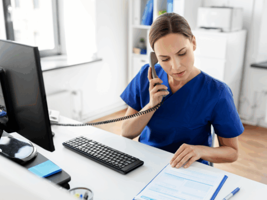 A nurse making a phone call and using the computer at the office desk.