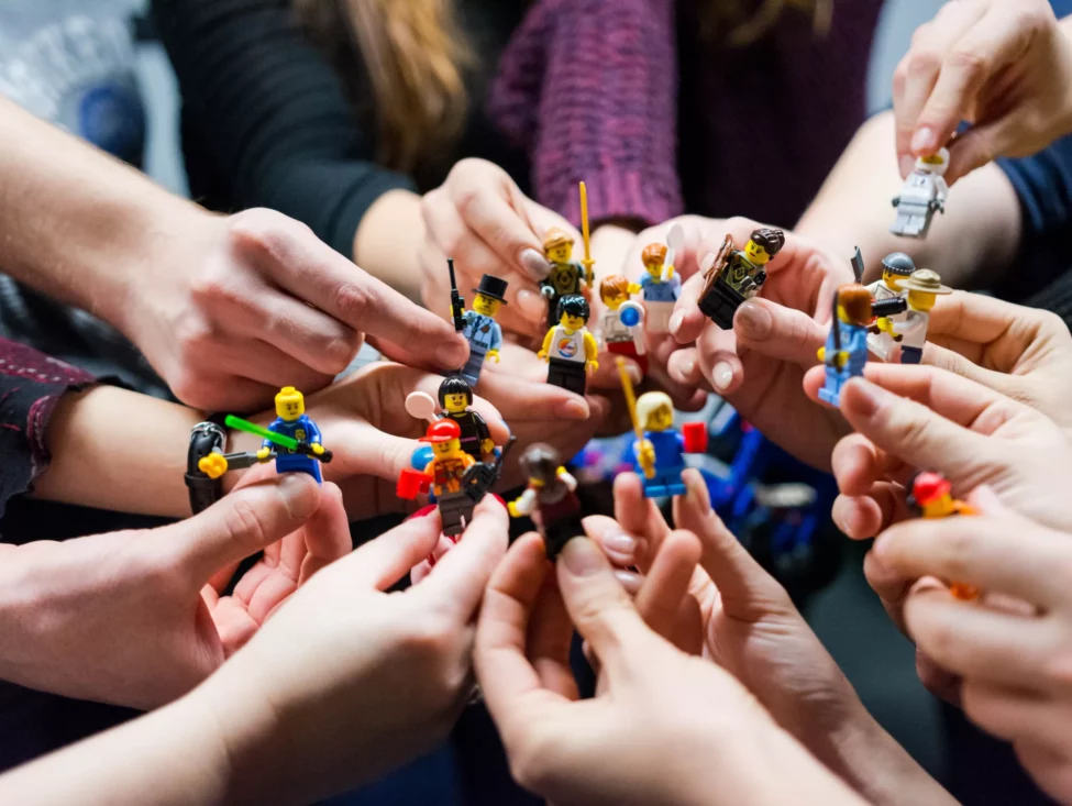 circle of hands all holding different lego characters